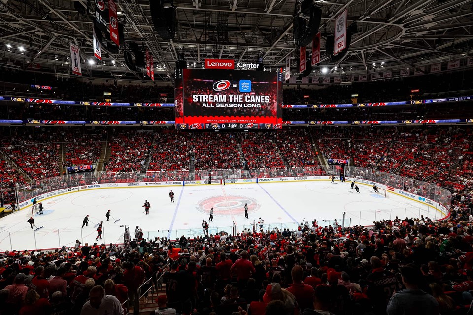 Fans fill Lenovo Center as the Carolina Hurricanes play on the ice beneath the arena’s central scoreboard.
