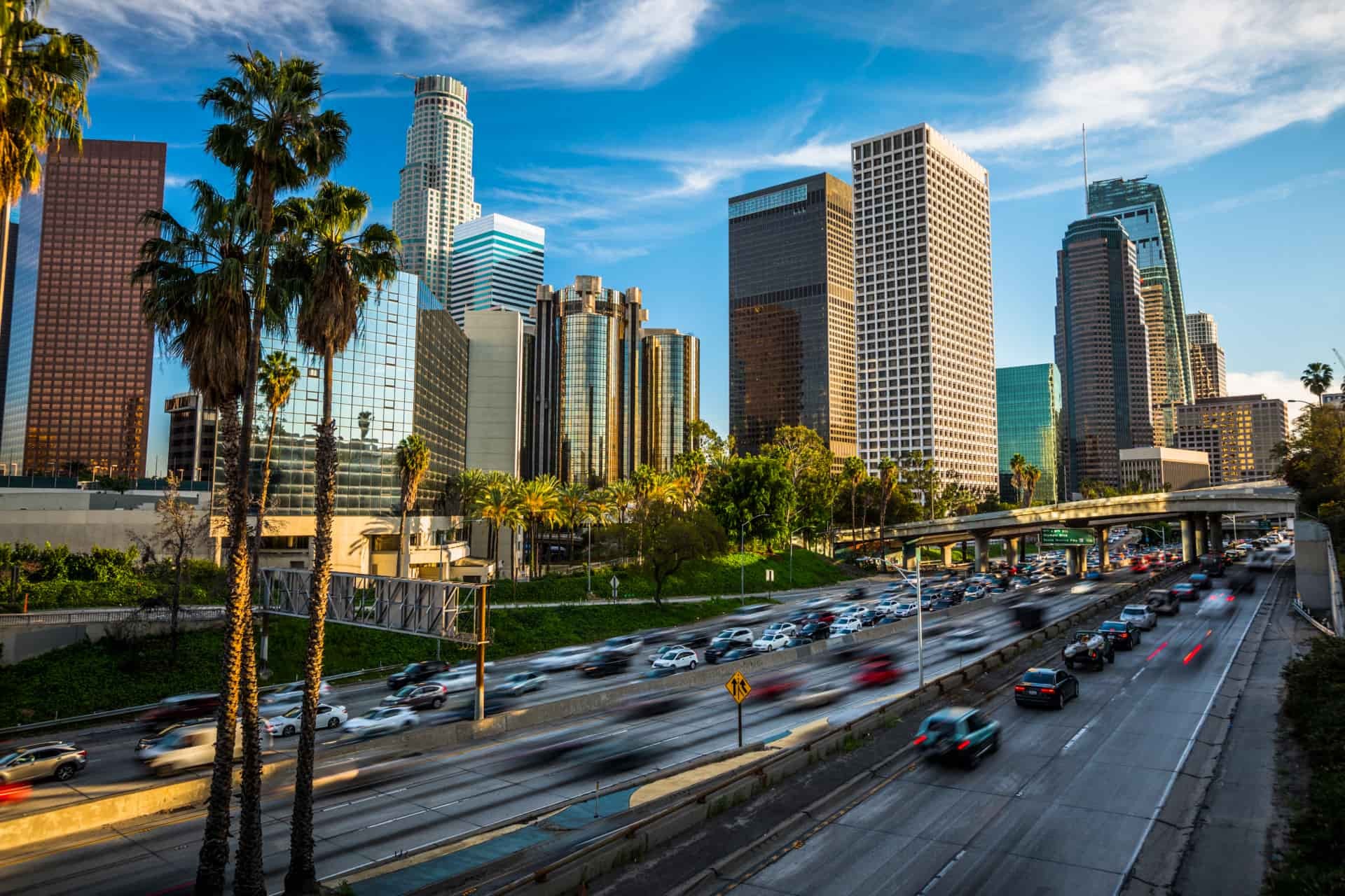 Downtown Los Angeles skyline with palm trees and traffic on a busy freeway.