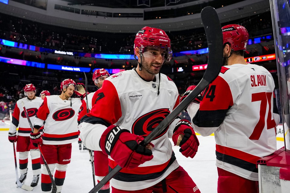 Carolina Hurricanes players in white and red uniforms step onto the ice, holding their hockey sticks.