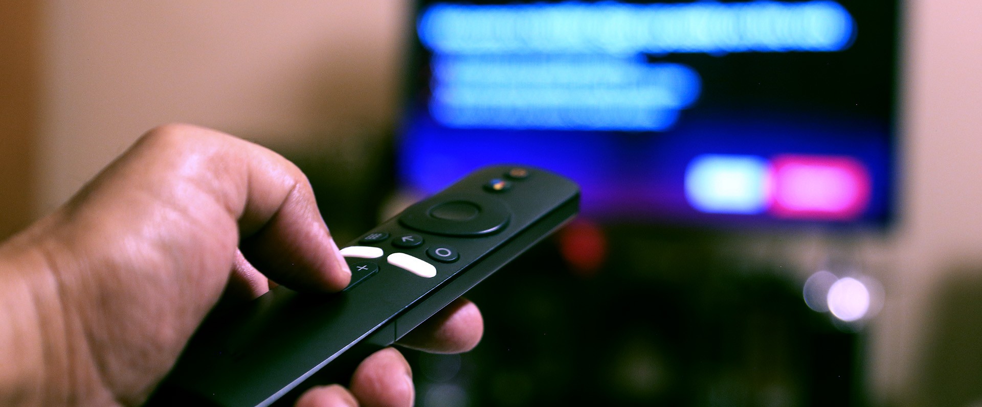 man's hand holding remote control with streaming tv in background